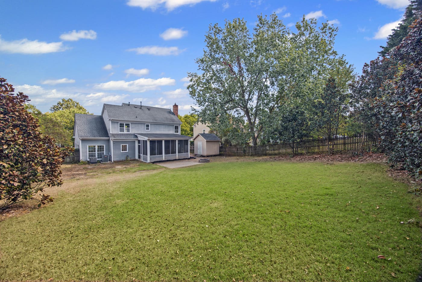 The fenced backyard lawn, with the rear of the house and screened porch in the distance.
