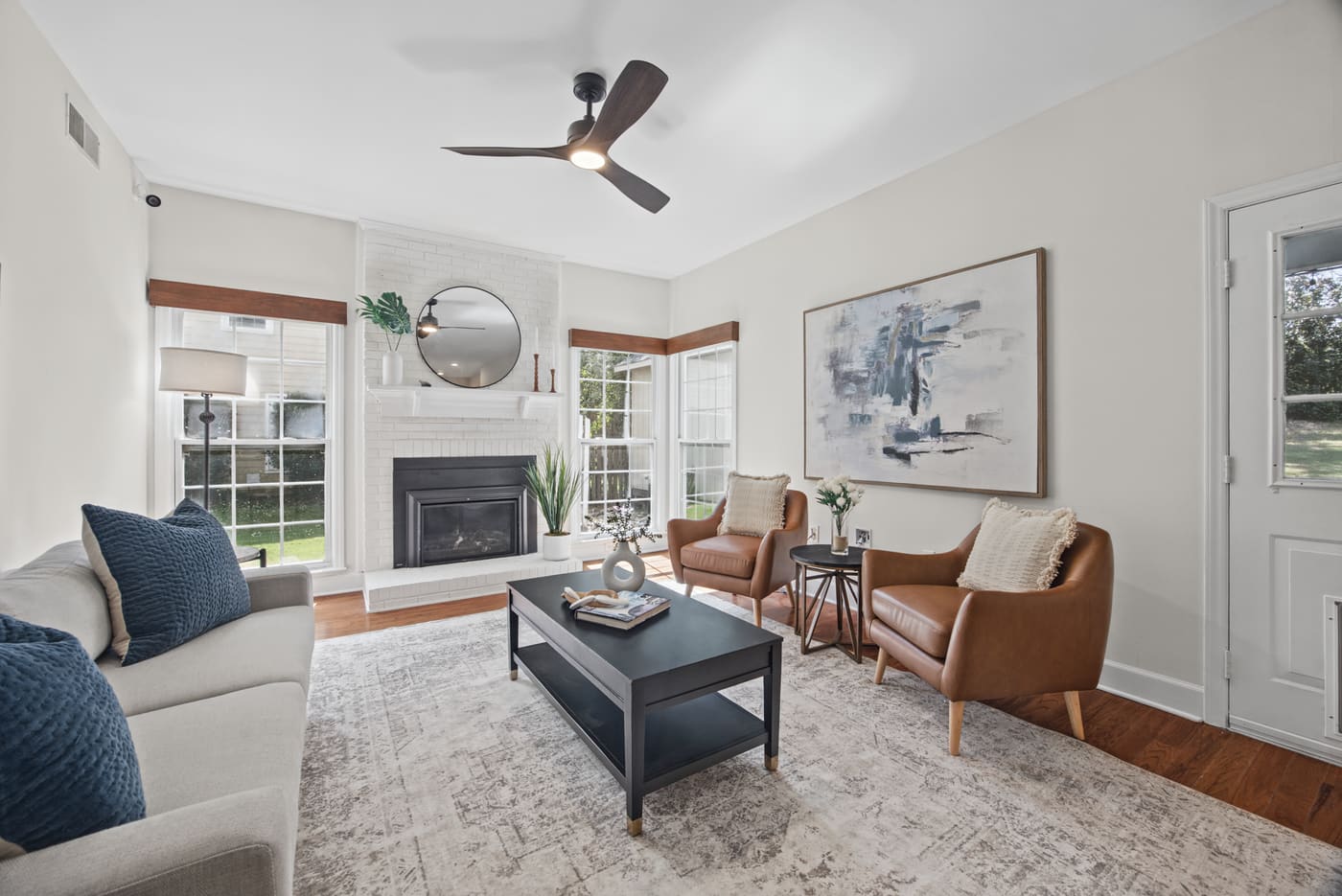 The family room with a white brick fireplace, a ceiling fan and windows on both sides.