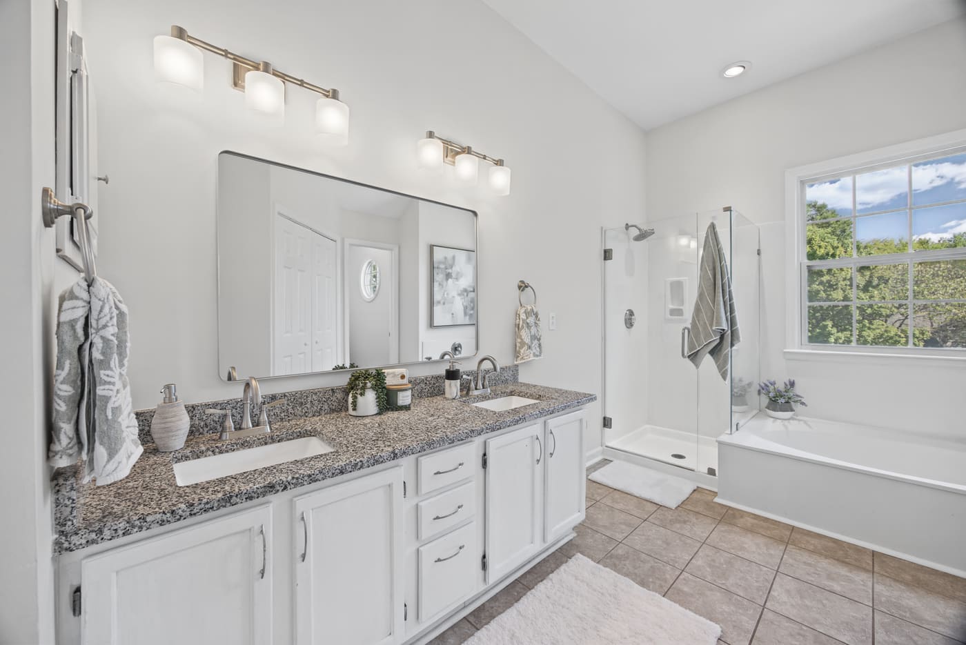 The primary bath with a double vanity, a glass shower and a soaking tub beneath a window.